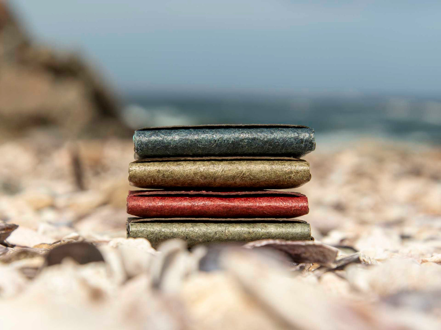 A striking scene featuring four distinct coloured wallets artfully stacked on a beach, emphasizing the compact and slender profile that defines our wallet design.